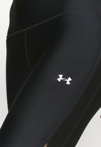 Czarne legginsy kompresyjne z gładką strukturą, płaskimi szwami oraz wyraźnym białym logo Under Armour z boku.