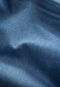 Nahaufnahme von blauem Denim-Stoff, der die detaillierte Webart und subtile Falten zeigt.