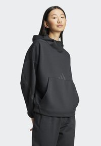 Crni sportski dukserica s visokim ovratnikom, prednjim džepom i diskretnim detaljem logotipa. Izrađena od mekanog materijala s opuštenim krojem.