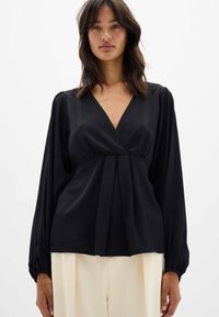 Blusa negra ajustada con un profundo escote en V, mangas largas abullonadas y detalles plisados en la cintura. Hecha de una tela suave y ligera.