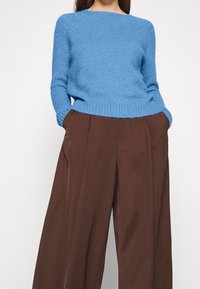 Maglione a maglia azzurro cielo con maniche lunghe e orlo a coste, abbinato a pantaloni a gamba larga marroni a vita alta, con tasche laterali.
