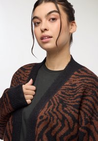 Dżersejowy kardigan w paski zebry w ciemnym brązie i czerni. Wykonany z miękkiej dzianiny, o luźnym kroju i szerokich rękawach. Okrągły dekolt.