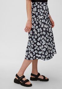 Falda midi floral en azul marino con patrones en blanco y azul. Cuenta con una cinturilla elástica y una forma fluida, combinada con sandalias negras.