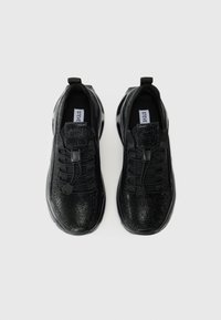 Chaussures de sport noires avec tissu en maille, tige texturée et lacets élastiques. Elles sont dotées d'une semelle rembourrée et d'une étiquette de marque sur la languette.