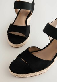 Sandali con zeppa in suede nero con piattaforma in corda, dotati di larghe cinturini incrociati e una fascia elastica alla caviglia per una vestibilità sicura.