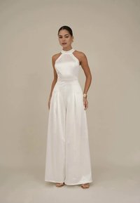 Macaquinho branco em cetim com decote halter, design de perna larga e textura suave. Apresenta um corte ajustado e detalhes plissados.