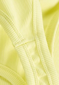 Tecido ribbed amarelo brilhante com textura suave. Costuras alinhadas criam um efeito de camadas, acentuando os detalhes do design da peça.