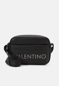 Black leather crossbody bag with silver "Valentino" logo, rectangular shape, adjustable strap, and smooth texture. Zipper closure on top.