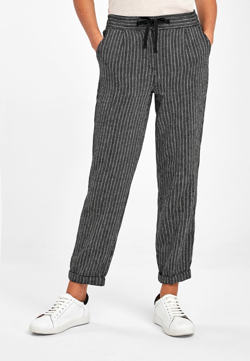 Pantalon décontracté à rayures verticales noires et blanches avec taille à cordon et chevilles resserrées, porté avec des baskets blanches.