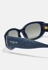 Mornarske sončne očala z sijajno površino; na shranjevanju nosilcev ima cvetlični reliéfni vzorec in zlato blagovno znamko "vogue". Gradientna stekla.
