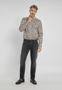 Koszula w kwiatowy wzór w jasnych odcieniach z kołnierzykiem zapinanym na guziki, zestawiona z ciemnoszarymi dżinsami i brązowymi mokasynami. Koszula ma luźny krój.