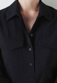 Camicia nera a maniche lunghe in tessuto testurizzato, con colletto, due tasche sul petto e bottoni a contrasto.