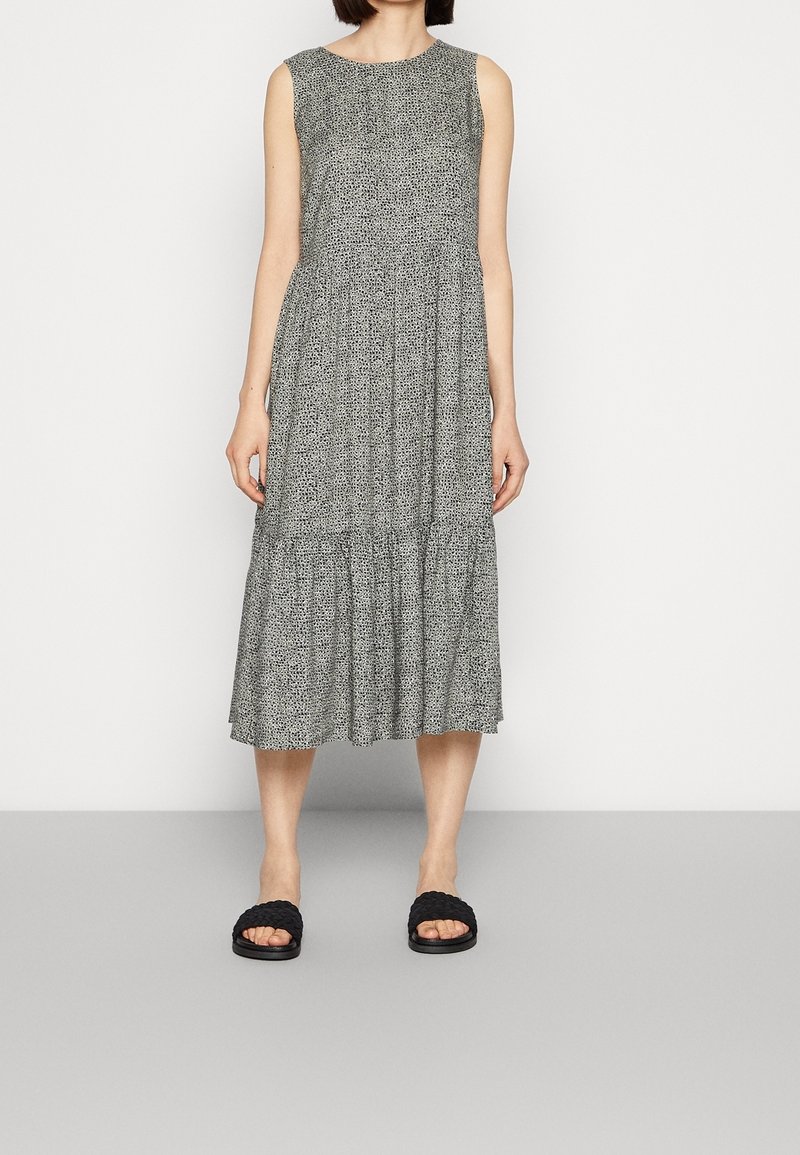 Robe midi grise sans manches à petits pois noirs, coupe ample et jupe à volants, portée avec des sandales plates tissées noires.