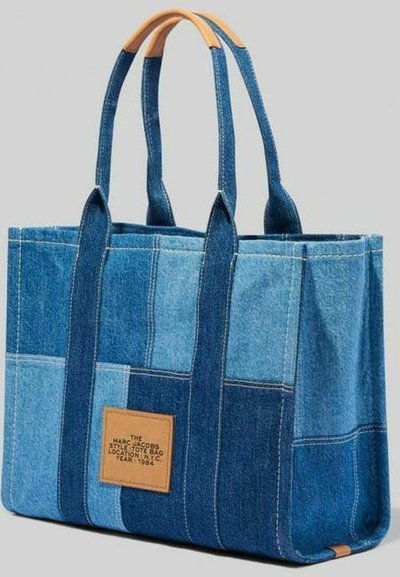 Borsa tote in denim con design patchwork in diverse tonalità di blu, dotata di due manici robusti e un'etichetta in pelle marrone su un lato.