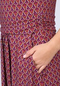 Lila gemustertes Kleid mit wellenförmigem Design in Pink- und Grüntönen, mit gerafftem Detail an der Taille und seitlichen Taschen.