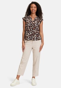 Blusa con stampa leopardata a maniche corte e chiusura con bottoni, abbinata a pantaloni tapered beige chiaro e sneakers bianche.