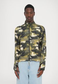 Camo-patterned zip jacket in green, beige, and gray shades. Features a high collar and thumbholes. Made from a lightweight, textured fabric.
