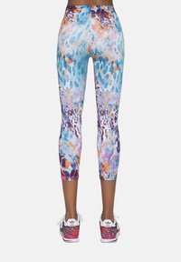 Kolorowe legginsy capri z abstrakcyjnym wzorem w odcieniach aqua, pomarańczowym i fioletowym o gładkiej fakturze, zestawione z różowo-czarnymi butami sportowymi.