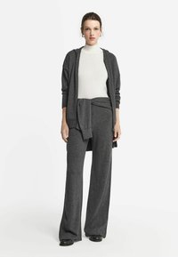 Grijze twee-delige outfit met losse broek en een lange cardigan, gecombineerd met een aansluitende witte coltrui, gemaakt van een zachte brei-stof.