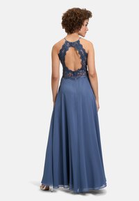 Robe longue bleue avec une jupe fluide. Dos en dentelle avec une découpe en forme de feston, bretelles réglables et texture lisse.