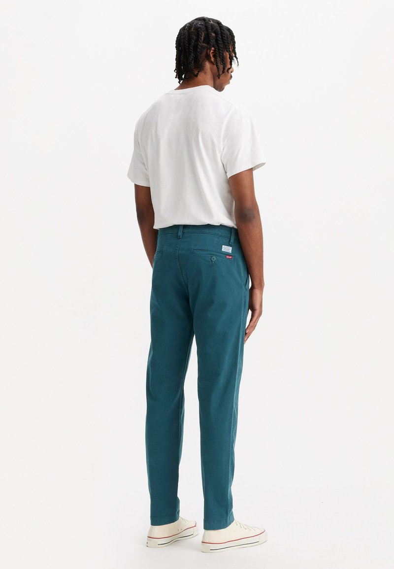Pantalon en coton vert d'eau avec une coupe droite, deux poches arrière et une petite étiquette de marque sur la taille, associé à un t-shirt blanc.