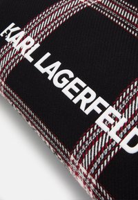 Svart rutigt tyg med vit "KARL LAGERFELD" logotyp. Har ett rutig mönster i röda, vita och grå toner för kontrast.