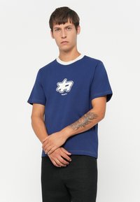 Mørkeblå bomulds T-shirt med rund hvid krave og korte ærmer. Har et fremtrædende hvidt og mørkeblåt logo på brystet.