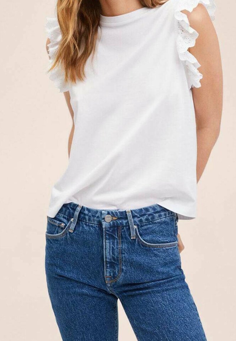 Witte mouwloze top met kantaccenten op de schouders, gecombineerd met hoge taille blauwe jeans met metalen knoop en een klassiek vijf-pocket ontwerp.