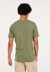 Žalias medvilninis marškinėliai su tekstūruotu paviršiumi, puikuojantis pasikartojančiu mažų transporto priemonių ir gyvūnų raštu keliomis spalvomis.