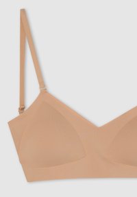 Reggiseno seamless di un beige chiaro con design a V, spalline regolabili e tessuto morbido e liscio. Presenta coppe sagomate per il supporto.
