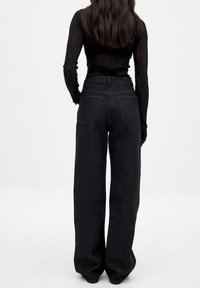 Mustad laiad teksad kõrge vöökoha ja kahe tagataskuga. Denimi tekstuur on sile ning neid on kombineeritud sobiva musta pika varrukaga särgiga.