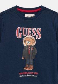 Sweatshirt azul-marinho com um gráfico de um urso num casaco preto, com realces em vermelho e o texto "LOS ANGELES EST. 1981" na parte inferior.