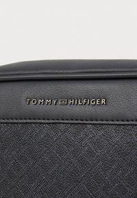 Sac à main en cuir noir avec une surface texturée et à motifs. Logo "Tommy Hilfiger" en métal doré sur le devant.