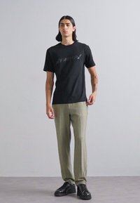 Black short-sleeve T-shirt with gray graphic print, paired with light green tailored pants and black lace-up shoes. Smooth fabric, relaxed fit.