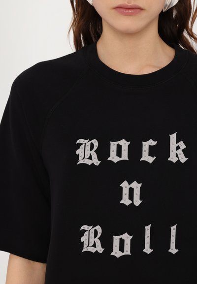 Sudadera negra con texto plateado tachonado que dice "Rock n Roll". Diseño casual con cuello redondo y mangas cortas raglán. Textura de tela suave.