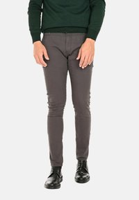 Pantaloni grigi slim-fit, realizzati in tessuto misto cotone, con una texture liscia e vita bassa, abbinati a scarpe di pelle nere.