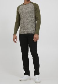 Långärmad tröja med rund halsringning som har en texturerad grå kropp och gröna raglanärmar. Tillsammans med svarta slim-fit jeans och vita sneakers.