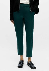 Teal tailored trousers with a smooth texture, featuring a straight cut and ankle length, paired with black patent loafers.