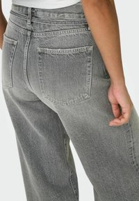 Jeans in denim grigio con vita alta, caratterizzati da un lavaggio sbiadito, due tasche posteriori e una vestibilità rilassata. Cuciture visibili lungo le tasche.