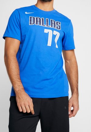 Mężczyzna w niebieskiej sportowej koszulce Dallas z numerem 77 i czarnych szortach Nike, stojący na jednolitym jasnym tle.