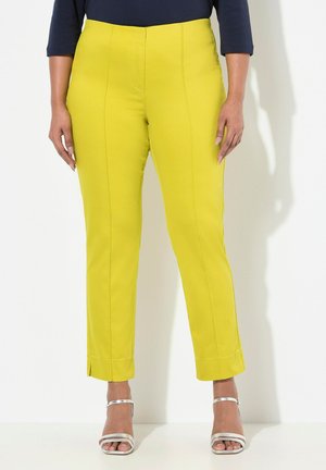 Pantalons jaunes fuselés avec une texture lisse et des détails de couture à l'avant, dotés d'un ourlet. Assortis à des sandales argentées à lanières.