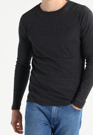 Czarna szara koszula z długim rękawem i dekoltem w serek, wykonana z teksturowanej tkaniny, w połączeniu z niebieskimi dżinsami. Skoncentrowana na dopasowaniu i jakości materiału.