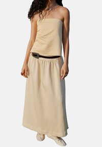 Haut tube beige associé à une longue jupe fluide beige. La tenue présente une taille cintrée avec une ceinture marron et une texture lisse.