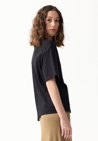 Czarna bawełniana koszulka, luźny krój, krótki rękaw i okrągły dekolt, zestawiona ze złotą, strukturalną spódnicą. Prosty i nowoczesny design.