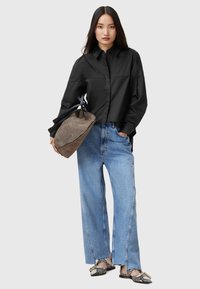 Camicia nera abbottonata, jeans in denim blu chiaro larghi, borsa a tracolla trapuntata grigia e scarpe basse con motivo bianco e nero. Texture morbide, look casual.