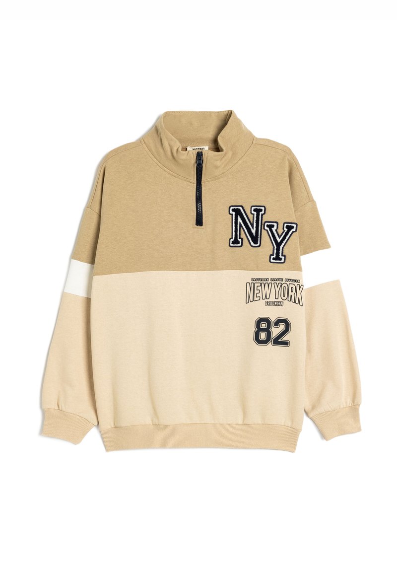 Pull en mélange de coton beige avec fermeture éclair à mi-hauteur, broderie noire "NY", rayures blanches et accents imprimés "NEW YORK" et "82" sur le devant.