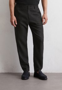 Zwarte linnen broek met een rechte pijp, knoopsluiting en een minimaal ontwerp. Draagt met zwarte instappers op een neutrale ondergrond.