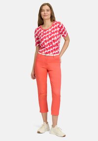 En kortærmet top i kornblomstblå med rosa mønster, parret med lys koralfarvede cropped bukser og hvide sneakers, der har et tyndt hvidt bælte.