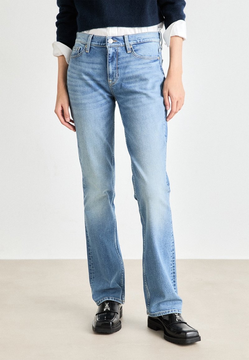 Jean bleu clair avec une coupe droite, en denim. Comprend un design classique à cinq poches et une légère décoloration. Porté avec des chaussures noires.