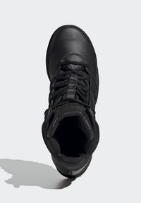 Chaussure montante noire en cuir texturé. Dispose d'un laçage et d'un col rembourré. La semelle est plate avec une légère inclinaison au niveau du talon.